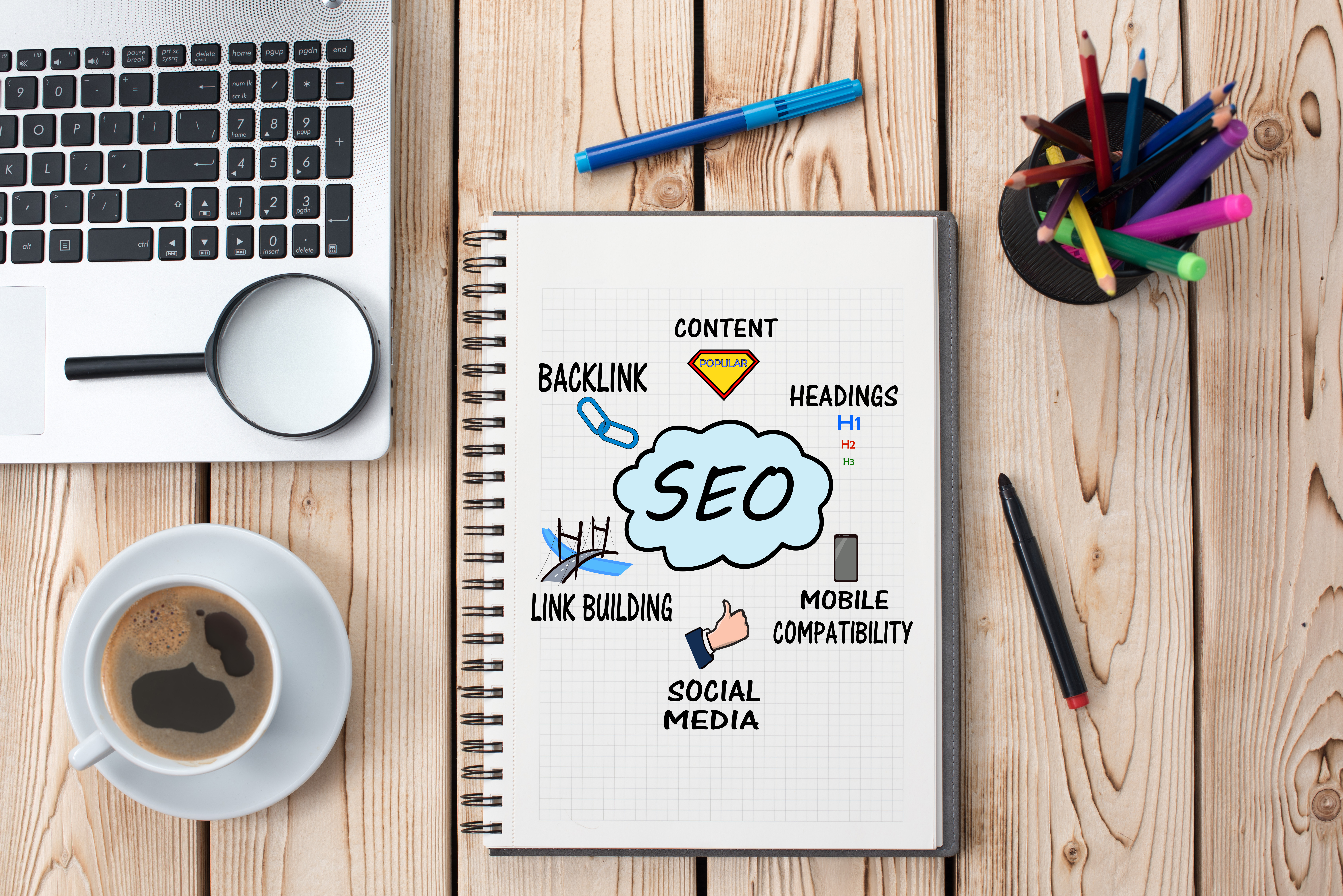 Notebook showing the letters SEO in a cloud, surrounded by the words 'content', 'headings', 'mobile compatibility', 'social media', 'link building' and 'backlink'